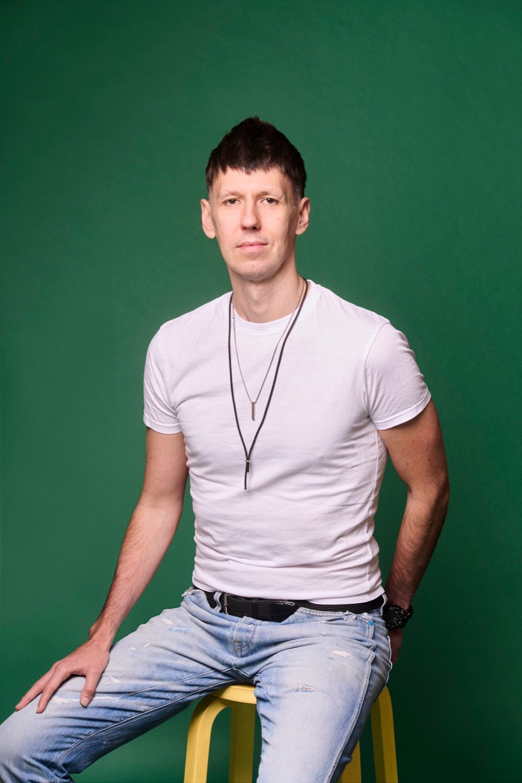 Jalmari Kivinen in a white T-shirt and jeans, sitting on a yellow stool in front of a green backdrop